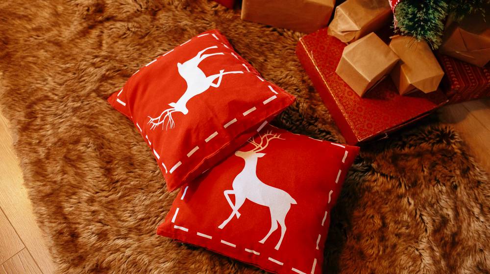 New Year's red pillows with deers lie near the Christmas tree on the floor | Decorative Christmas Pillows For Cozy And Festive Holiday Furnishing | Featured | decorative xmas pillows