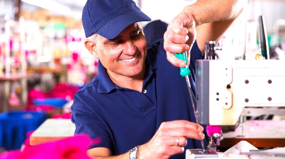 senior mechanic repairing industrial sewing machine | Sewing Machine Repair Cost Guide