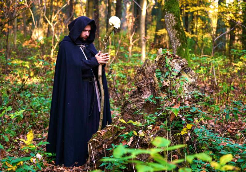 man wearing cloak and holding a wooden cane with white skull ornament | fantasy sewing patterns