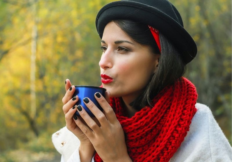 Beautiful woman in a white coat, crochet Red scarf and black hat holds a cup in her hands | free crochet scarf patterns