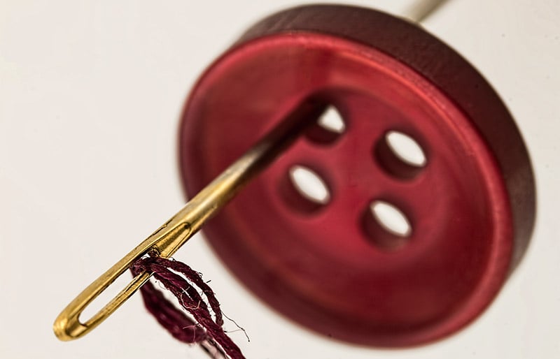 brass needle through red cloth button | basic sewing skills
