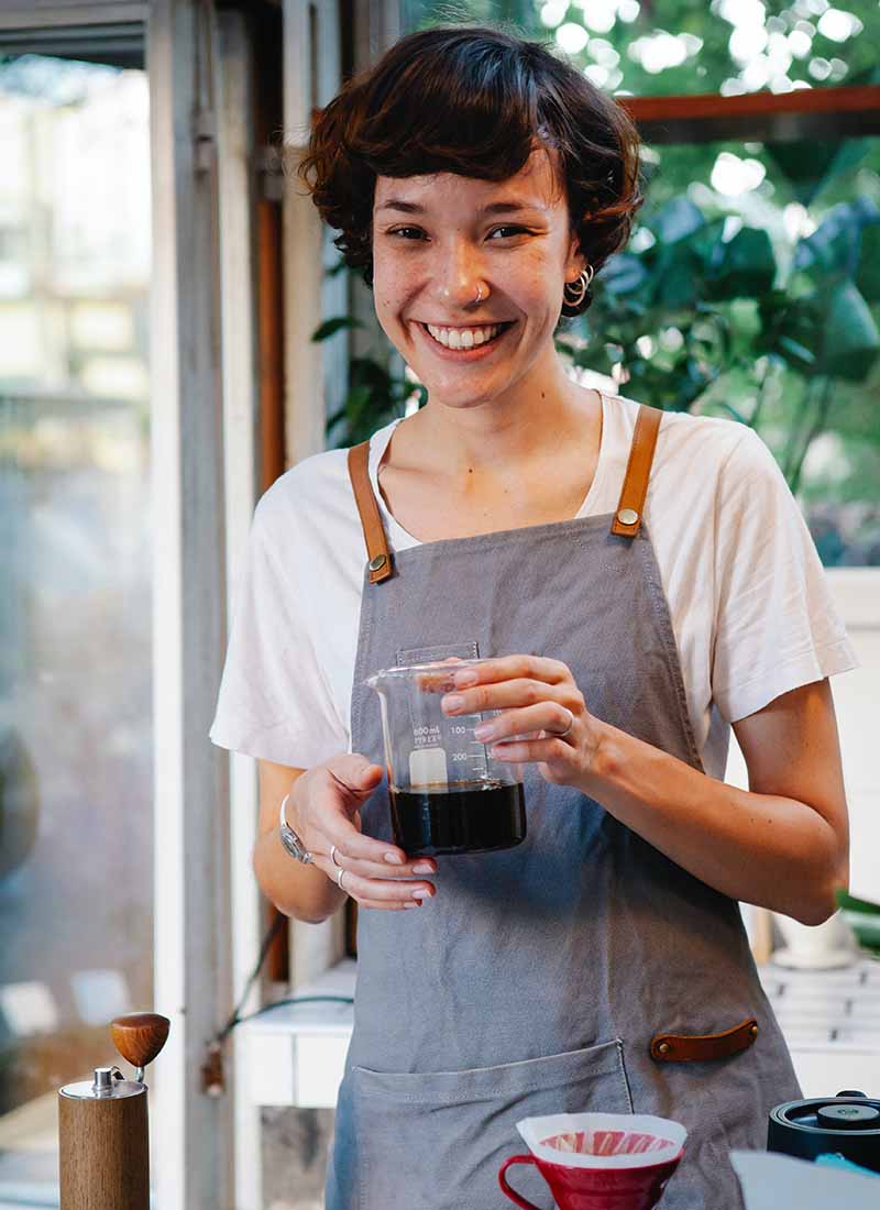 happy woman in apron with jug of coffee smiling at camera | apron pattern