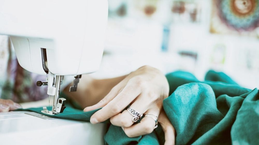 person sewing green textile using white electric sewing machinge | The Best Sewing Machine For Beginners Guide | Featured
