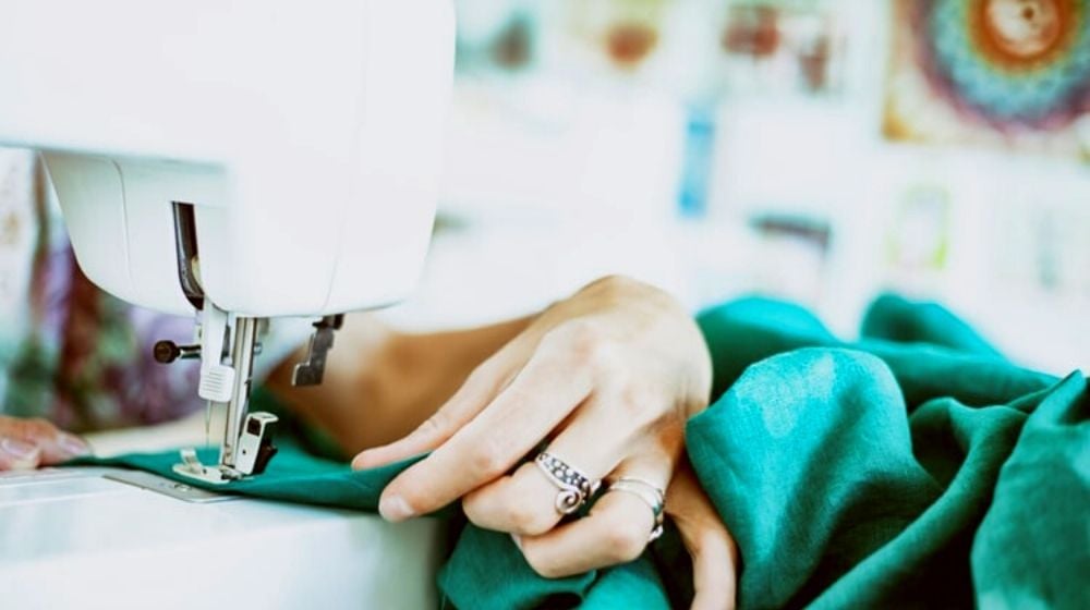 person sewing green textile using white electric sewing machine | Basic Sewing Machine Parts Every Beginner Should Know
