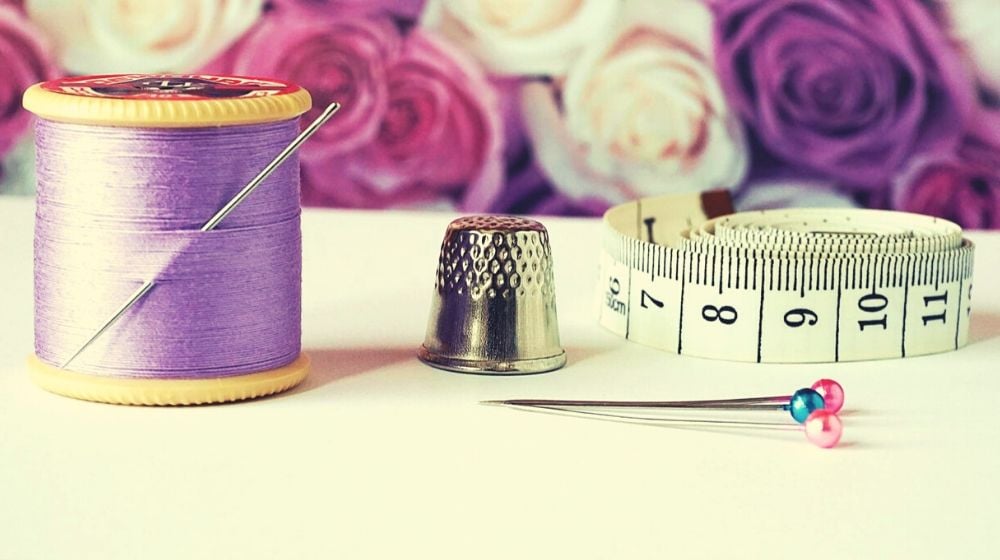 thimble purple thread measuring tap needle pins and pink and purple flowers | How to Sew By Hand In 6 Easy Steps
